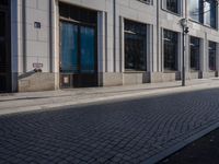 a sidewalk with a bench and brick sidewalk and building with a sky background and reflection on water