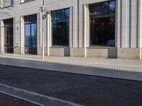 a sidewalk with a bench and brick sidewalk and building with a sky background and reflection on water