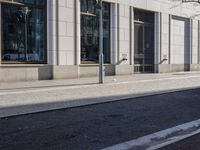 a sidewalk with a bench and brick sidewalk and building with a sky background and reflection on water