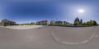 a fisheye lens captures the view from an empty road in a city park with a skateboarder going down a half pipe