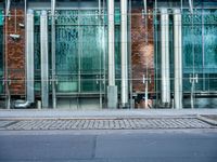 a person walks by a large metal pole near an open brick and glass building with glass walls