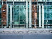 a person walks by a large metal pole near an open brick and glass building with glass walls