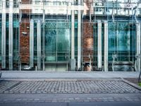 a person walks by a large metal pole near an open brick and glass building with glass walls