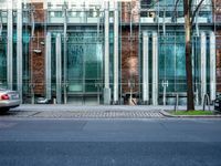 a person walks by a large metal pole near an open brick and glass building with glass walls