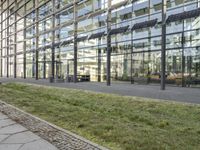 the building has glass walls and a sidewalk with green grass in it outside of it