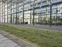 the building has glass walls and a sidewalk with green grass in it outside of it