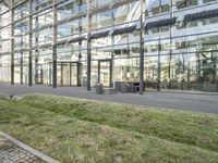 the building has glass walls and a sidewalk with green grass in it outside of it