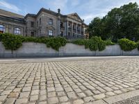 the front of a mansion surrounded by trees and stone floors in a parking lot, near a street