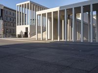 the large, empty sidewalk with multiple columns in front of the building with two signs