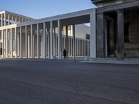 the large, empty sidewalk with multiple columns in front of the building with two signs