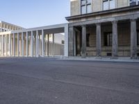 the large, empty sidewalk with multiple columns in front of the building with two signs