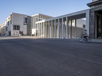 the large, empty sidewalk with multiple columns in front of the building with two signs