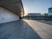 a skateboarder riding on a cement ramp next to a city street under a bridge