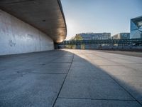 a skateboarder riding on a cement ramp next to a city street under a bridge