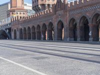 an empty road with large stone walls and towers on it in an urban setting, with buildings lining the streets and trolley tracks passing by