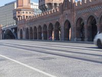 an empty road with large stone walls and towers on it in an urban setting, with buildings lining the streets and trolley tracks passing by