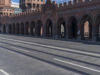 an empty road with large stone walls and towers on it in an urban setting, with buildings lining the streets and trolley tracks passing by