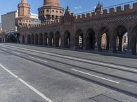 an empty road with large stone walls and towers on it in an urban setting, with buildings lining the streets and trolley tracks passing by