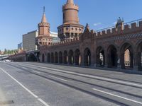 an empty road with large stone walls and towers on it in an urban setting, with buildings lining the streets and trolley tracks passing by