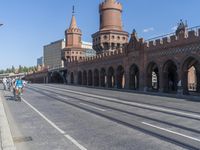 an empty road with large stone walls and towers on it in an urban setting, with buildings lining the streets and trolley tracks passing by