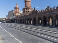 an empty road with large stone walls and towers on it in an urban setting, with buildings lining the streets and trolley tracks passing by