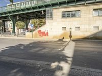 a shadow of a person on the sidewalk next to a building with a bridge above it