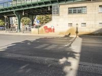 a shadow of a person on the sidewalk next to a building with a bridge above it