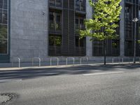 a building along a street lined with a fence in the center of it and a small tree lining the sidewalk