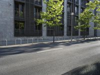 a building along a street lined with a fence in the center of it and a small tree lining the sidewalk