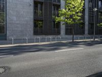 a building along a street lined with a fence in the center of it and a small tree lining the sidewalk