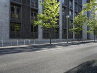 a building along a street lined with a fence in the center of it and a small tree lining the sidewalk