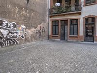 a building with graffiti in a brick alley behind it and a doorway to the right