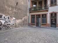 a building with graffiti in a brick alley behind it and a doorway to the right