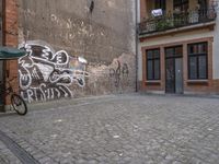 a building with graffiti in a brick alley behind it and a doorway to the right