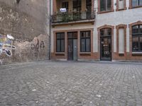 a building with graffiti in a brick alley behind it and a doorway to the right