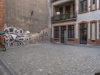 a building with graffiti in a brick alley behind it and a doorway to the right