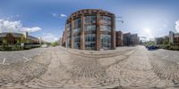 fisheye photograph with street in background and several buildings in back ground and sky with clouds