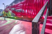 a painted stairway leading up to a ramp in front of a colorful building, with red curtain at the top