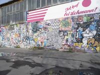 the large painted wall near a building is surrounded by stickers and signs that say