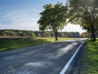 two children riding a bicycle on a paved road next to green grass and trees under blue skies