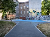 a basketball court and some graffiti on it in front of a building with trees and grass