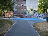 a basketball court and some graffiti on it in front of a building with trees and grass