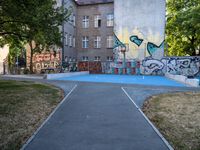 a basketball court and some graffiti on it in front of a building with trees and grass