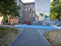 a basketball court and some graffiti on it in front of a building with trees and grass