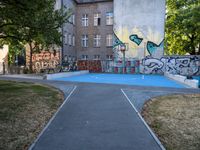 a basketball court and some graffiti on it in front of a building with trees and grass