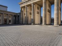 a large white building with pillars and some people walking around it and the ground with an open area