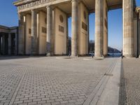 a large white building with pillars and some people walking around it and the ground with an open area