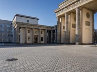 a large white building with pillars and some people walking around it and the ground with an open area
