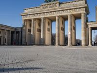 a large white building with pillars and some people walking around it and the ground with an open area