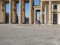 a large white building with pillars and some people walking around it and the ground with an open area